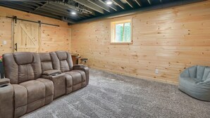 A cozy room with a brown leather sectional sofa, a gray bean bag, and a wooden wall with a window. - Hideaway Pines Cabin (Logan)