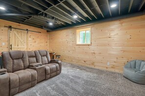 A cozy room with a brown leather sectional sofa, a gray bean bag, and a wooden wall with a window.