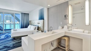 Een moderne hotelkamer met een groot bed, een aparte badkamer met een wastafel en uitzicht op de stad.