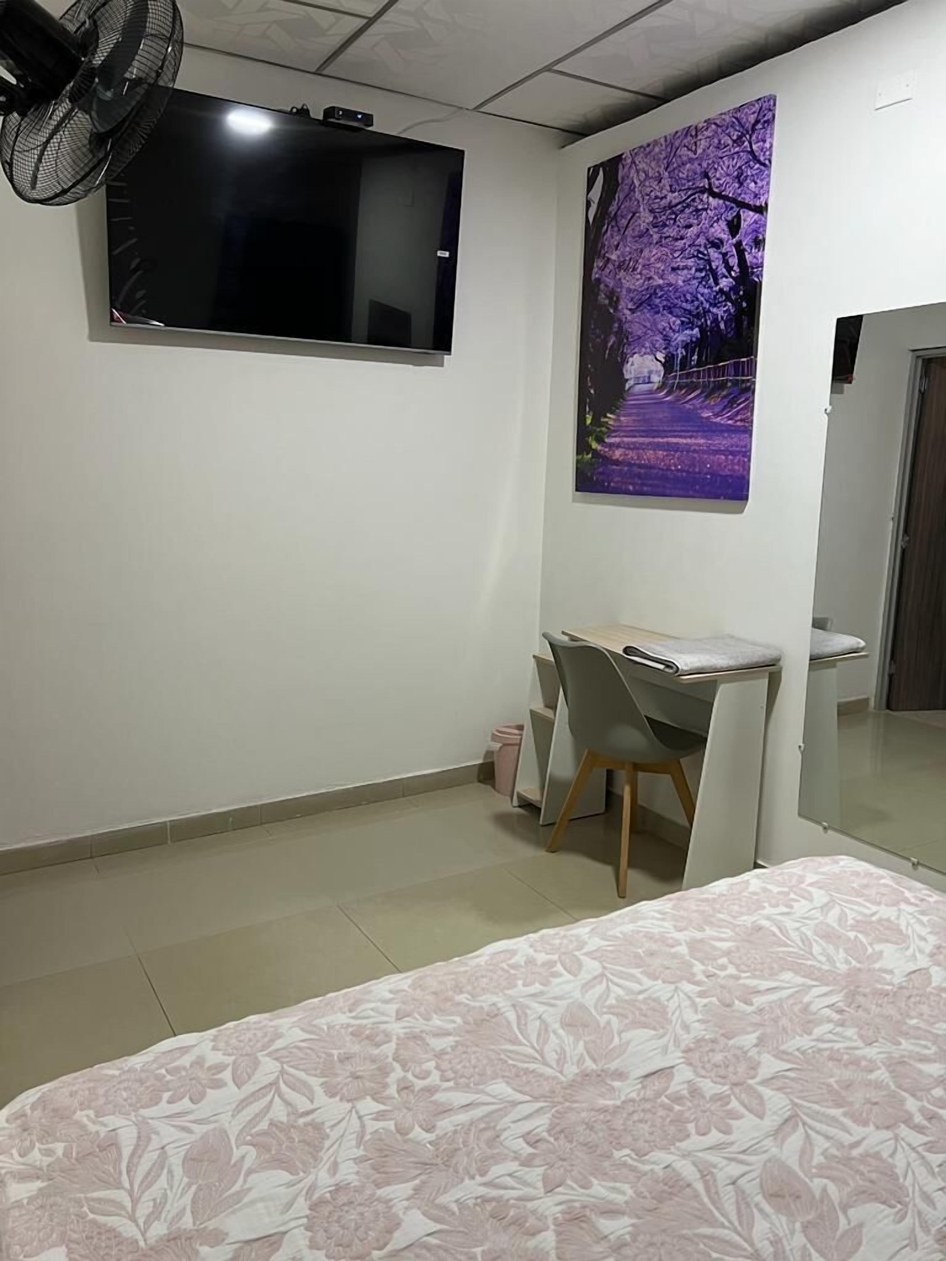A bedroom with a bed, a desk, a chair, a TV, and a poster on the wall.