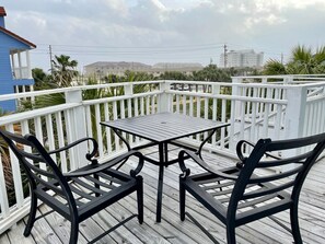 Une terrasse en bois avec une table et deux chaises, entourée de rampes blanches.