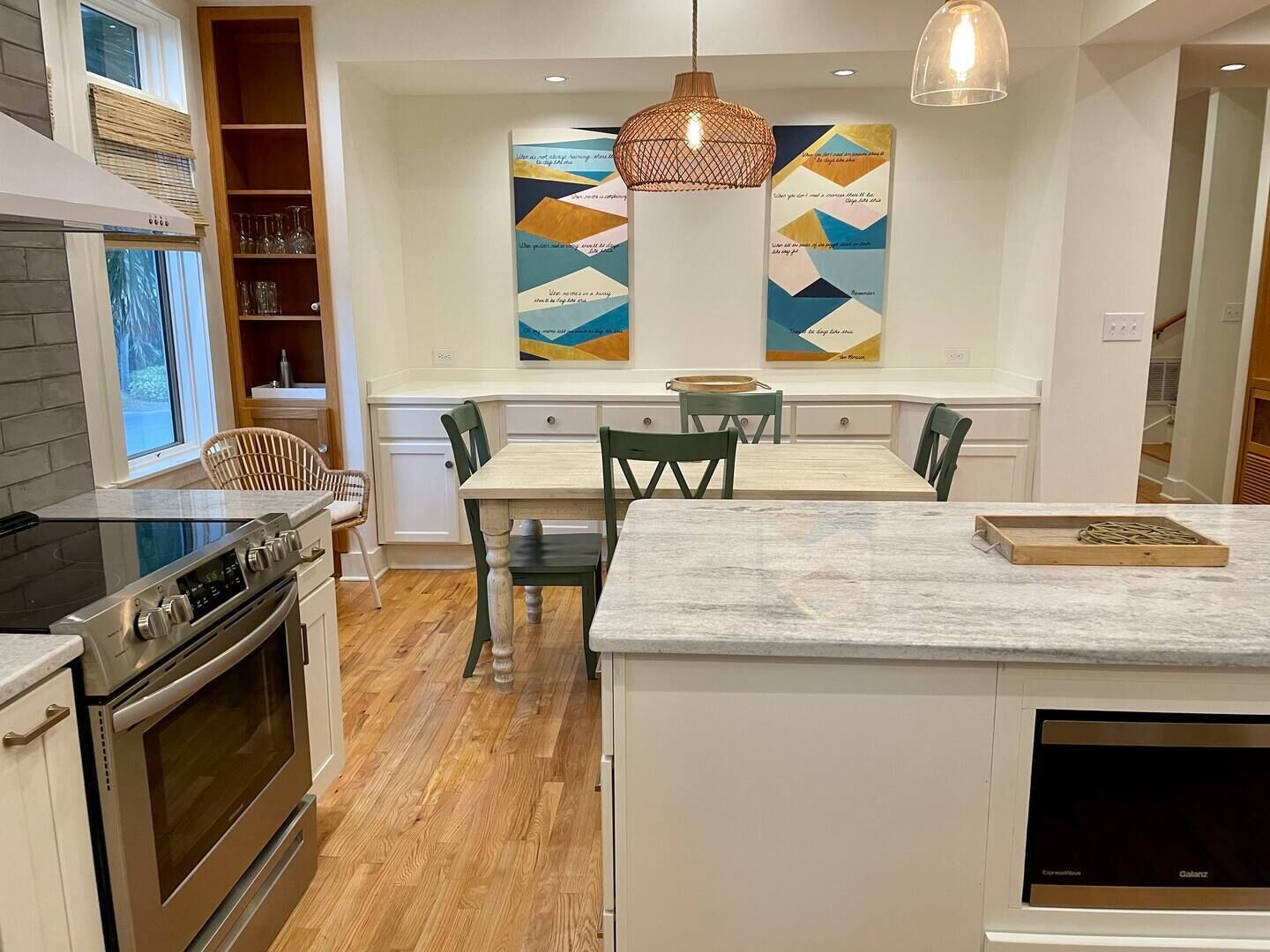 A modern kitchen with a central island, wooden flooring, and pendant lighting.