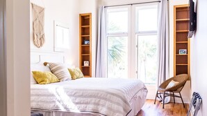 Una camera da letto con un letto, una sedia, un pannello decorativo in macramè e una scaffalatura in legno.