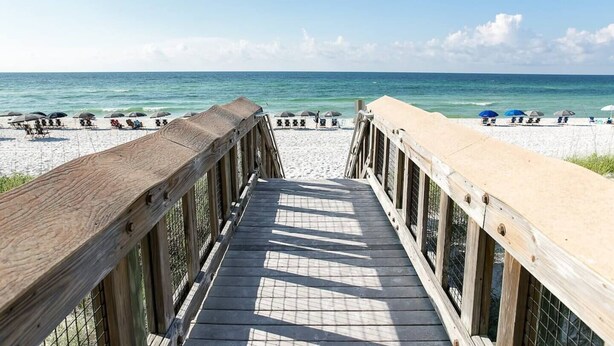 Una passerella in legno che conduce a una spiaggia con ombrelloni e sedie.