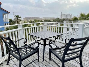 A wooden deck with a table and two chairs, surrounded by white railings.