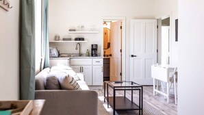 Una sala de estar moderna con un sofá, una mesa de centro, y una zona de cocina visible a través de una puerta abierta.