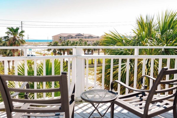 A balcony with two chairs and a small table, overlooking a beach and a building.
