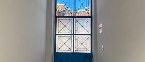 A hallway with a blue door, a tiled floor, and a window with a view of buildings.