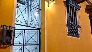 A yellow building with a large window featuring intricate metalwork and a blue door. - banana hostel (Bogotá)