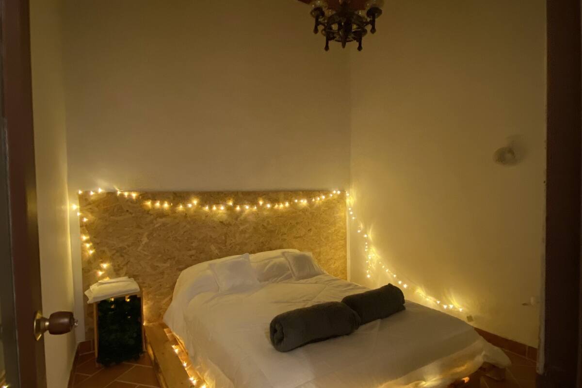 A bedroom with a wooden bed, white linens, a stone wall, and string lights.