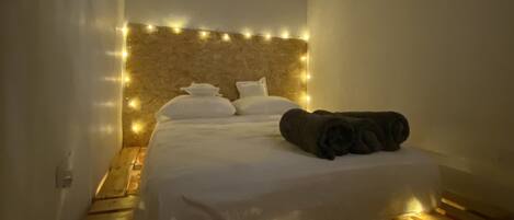 Un dormitorio con cama, cabecera iluminada, banca de madera y candelabro.