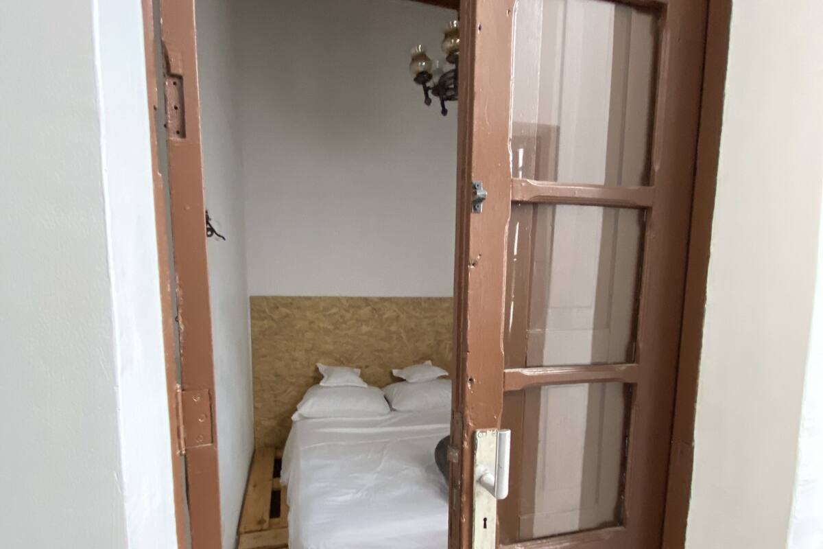 A narrow doorway leading to a bedroom with a wooden bed frame and white bedding.