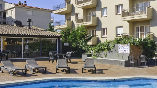 A pool area with lounge chairs, a bar, and a building with multiple balconies. - APCOSTAS Tropik / Two Bedrooms (L'Estartit)