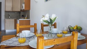 Ett matbord med frukostmat, en vas med vita blommor och ett kök i bakgrunden.