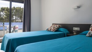 Ett hotellrum med två sängar, ett litet bord med stolar, ett fönster med gardiner och utsikt över träd utanför.