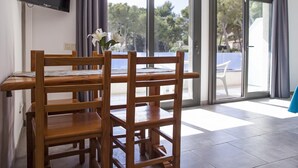 A modern room with a wooden dining table and chairs, a flat-screen TV mounted on the wall, and large sliding glass doors leading to an outdoor area.