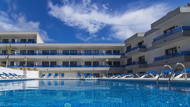 A hotel with a swimming pool, multiple balconies, and a clear blue sky.
