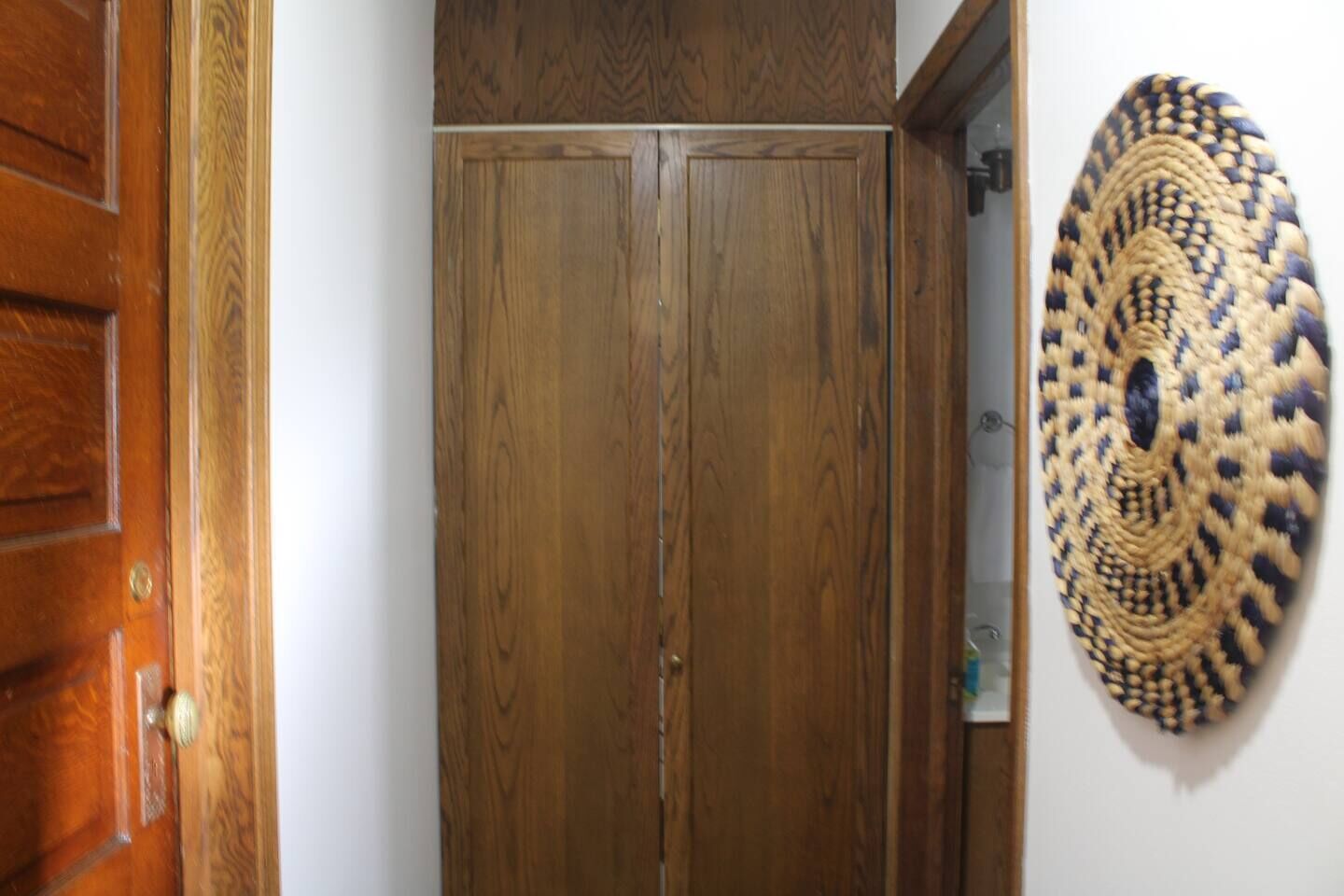 A wooden door with a simple design, a woven wall hanging, and a small shelf with items.