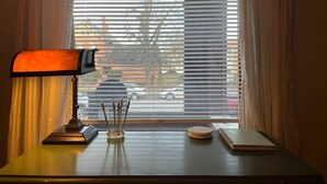 A desk with a lamp, a notepad, and a pen holder by a window with blinds.
