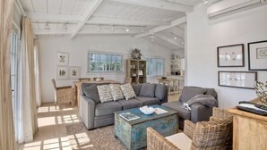A spacious living room with a high ceiling, a gray sofa, a coffee table, and wicker furniture. - Walk To Beach & Village | 5 Bedrooms | 3 Units (Carlsbad)