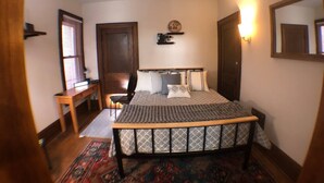Une chambre à coucher comprenant un lit, un bureau, une chaise, une fenêtre avec des stores, une porte et un luminaire fixé au mur.
