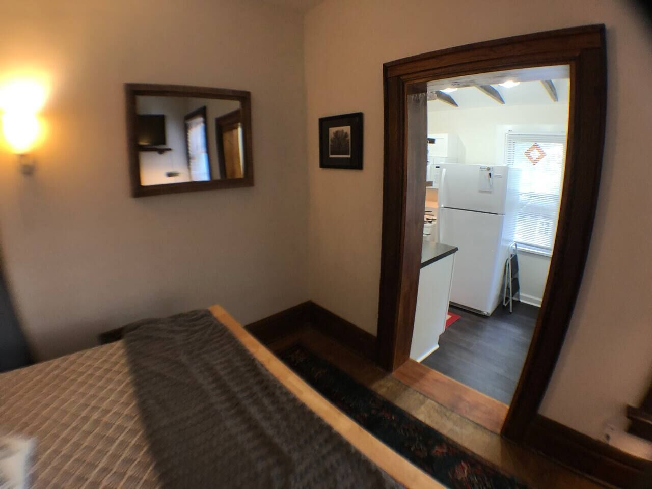 A bedroom with a bed, a mirror, and a door leading to a kitchen.