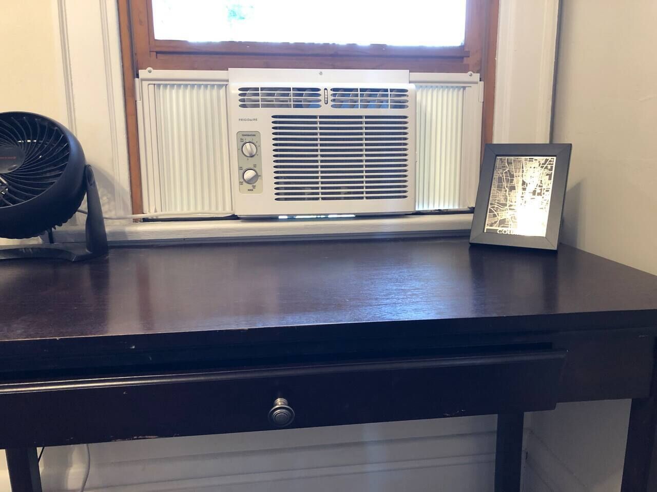A desk with a radiator, a fan, and a framed map.