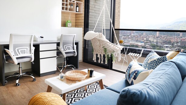 Una sala moderna con un sofá, sillas, una mesita de centro y un sillón colgante. Se aprecia una vista panorámica de la ciudad a través de amplios ventanales.
