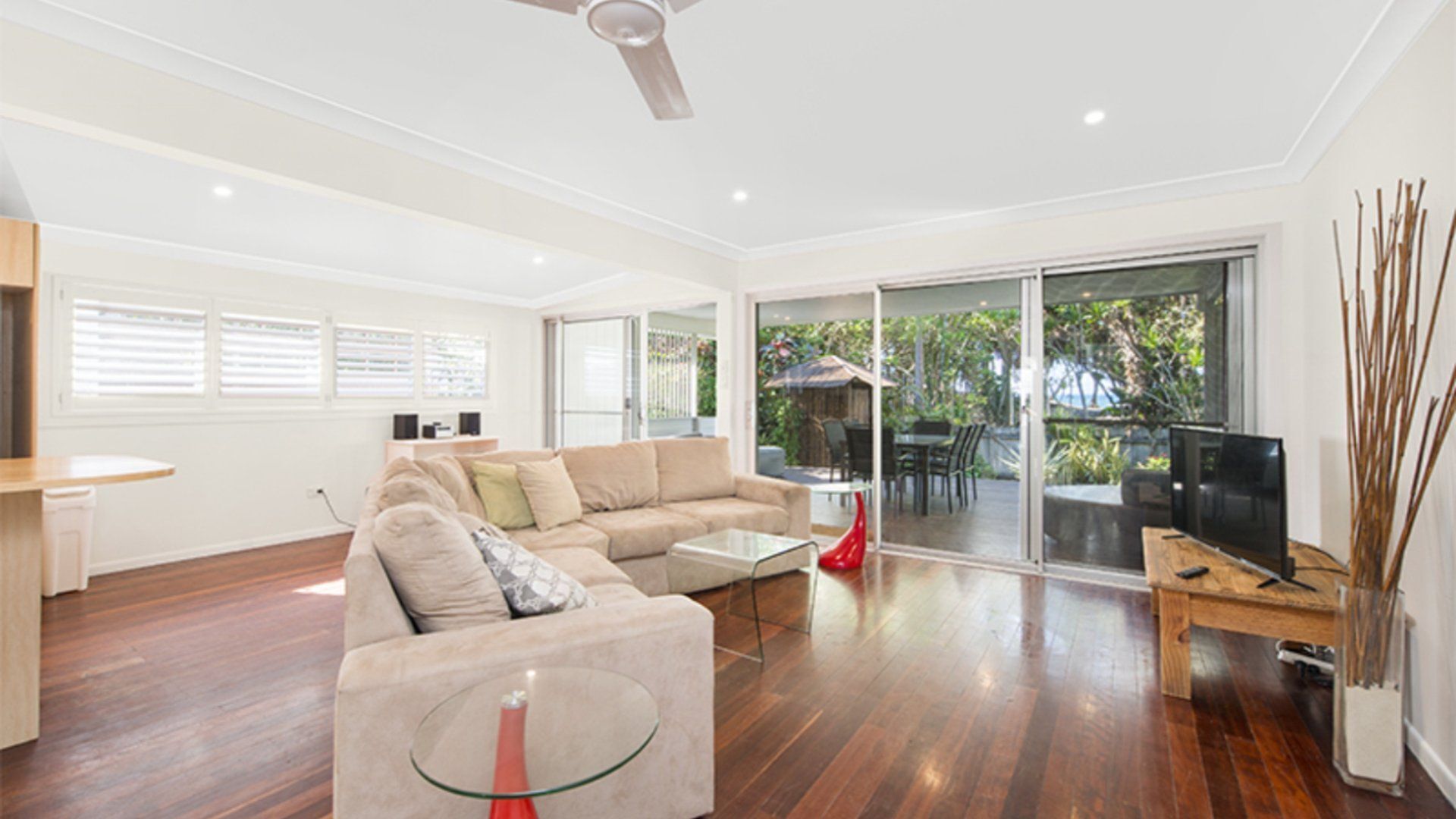 A spacious living room with a large sofa, a glass coffee table, and a television on a wooden stand.