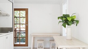 A kitchen with a wooden door, a white countertop, and a white table with two stools. - Whalesong - by Lifestyle. Brunswick Heads (NEW BRIGHTON)
