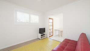 A room with a television on a white stand, a red couch, and a yellow patterned rug. - Whalesong - by Lifestyle. Brunswick Heads (NEW BRIGHTON)