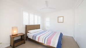 A bedroom with a bed, a nightstand, a ceiling fan, and a window with blinds. - Whalesong - by Lifestyle. Brunswick Heads (NEW BRIGHTON)