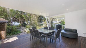 An outdoor dining area with a table and chairs, surrounded by a wooden deck and greenery. - Whalesong - by Lifestyle. Brunswick Heads (NEW BRIGHTON)
