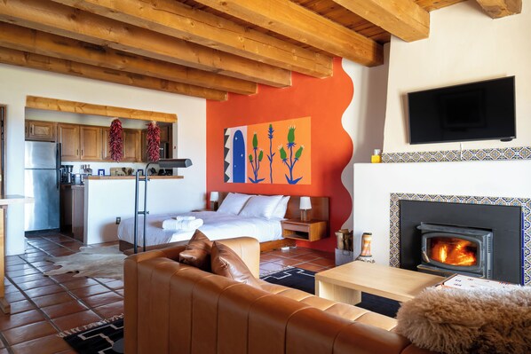 A modern interior with a wooden ceiling, a bed, a sofa, a fireplace, and a kitchen area.