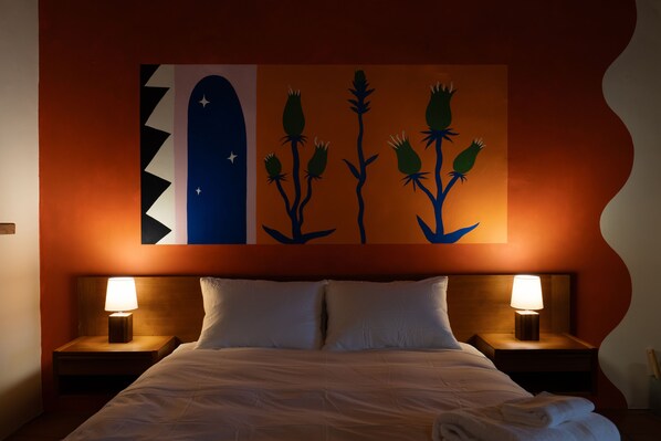 A hotel room with a bed, two bedside tables with lamps, and a wall with a colorful abstract painting.
