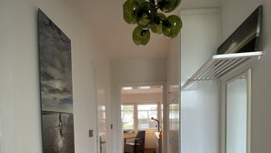 Ein Flur mit Holzboden, einem Bild an der linken Wand, einer Deckenleuchte und einem Fenster im Hintergrund.