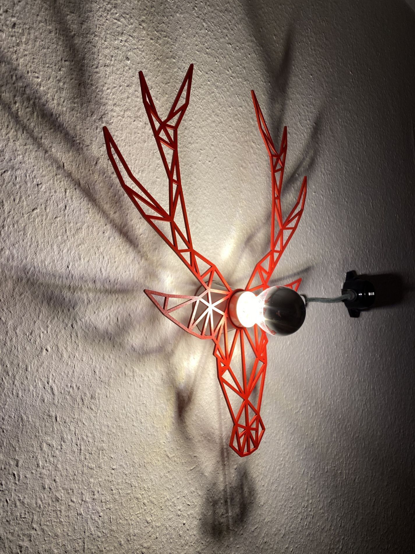 Ein Deckenventilator mit geometrischem, rotem Design, an einer strukturierten Wand befestigt.