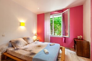 A bedroom with a bed, bedside lamp, window with curtains, and a wooden bench.