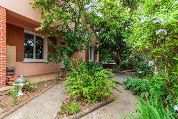 A building with a brick facade, a window, and a garden with various plants and a decorative urn.