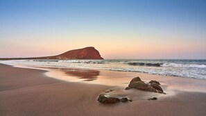 Una spiaggia con una roccia imponente, onde e cielo sereno.