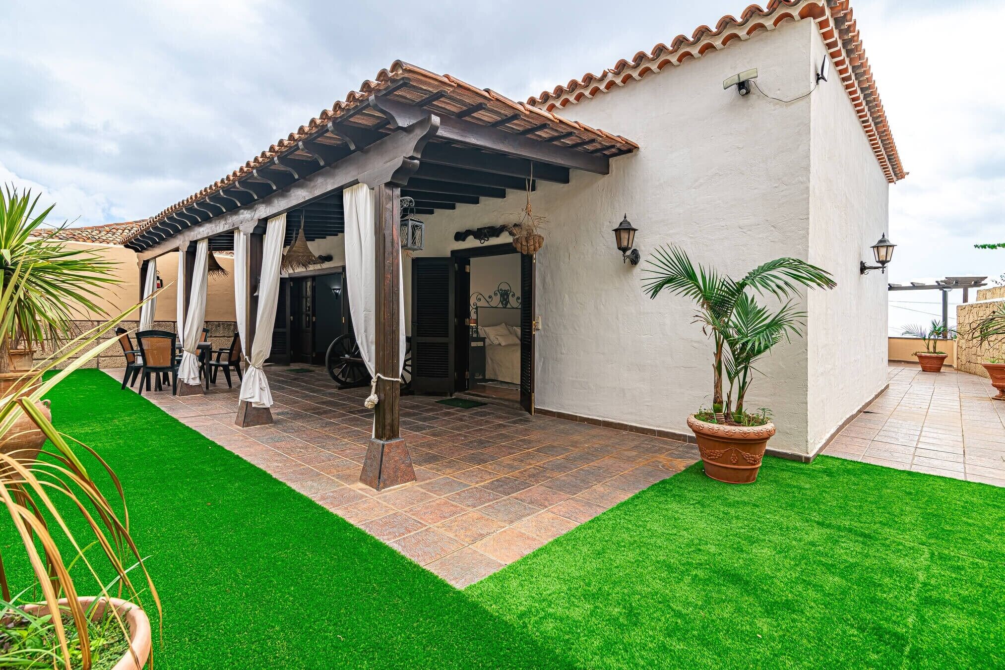 Ein überdachter Patio-Bereich mit einer Pergola, Sitzgelegenheiten im Freien und einem gepflegten Rasen.