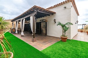 Un'area patio coperta con un pergolato, posti a sedere all'aperto e un prato curato.
