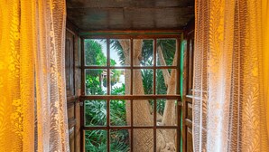 A window with a grid pattern, framed by wooden panels, overlooking a lush garden with various plants and trees. - Holiday Home "Bernarda" with Heated Pool, Sea Views, Private Pool and Wi-Fi (Villa de Arico)