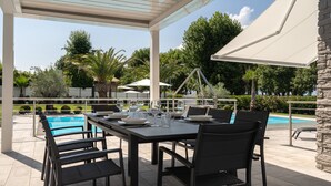 Une terrasse extérieure avec une piscine, une table à manger, des chaises et des parasols.
