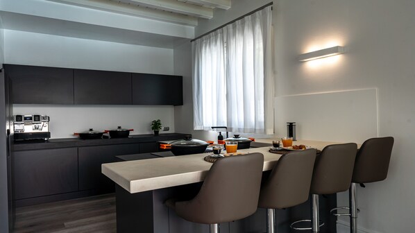 A modern kitchen with a bar area, featuring a coffee machine, a fruit bowl, and a breakfast setting.