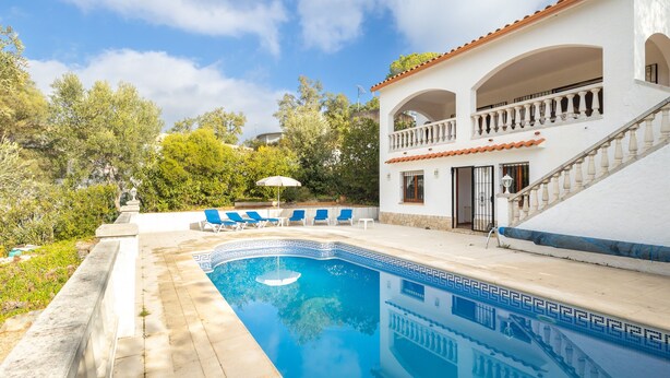 A swimming pool with a geometric tile pattern, a white building with a red-tiled roof, and a balcony with blue chairs. - Holiday Home 'La Calma' with Mountain View, Wi-Fi (Calonge)