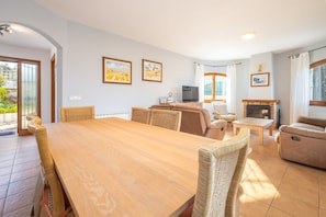 A spacious living area with a wooden dining table, wicker chairs, a sofa, a fireplace, and a television. - Holiday Home 'La Calma' with Mountain View, Wi-Fi (Calonge)