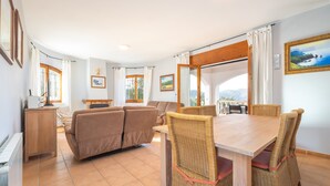 A dining area with a wooden table and wicker chairs, a sofa, and a view through an arched window. - Holiday Home 'La Calma' with Mountain View, Wi-Fi (Calonge)