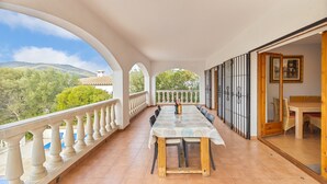 A balcony with a table and chairs, a view of trees and hills, and a door leading to an interior room. - Holiday Home 'La Calma' with Mountain View, Wi-Fi (Calonge)