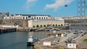 Ein Gebäude am Wasser mit einem Steg, einem großen Parkplatz und einer Brücke im Hintergrund.